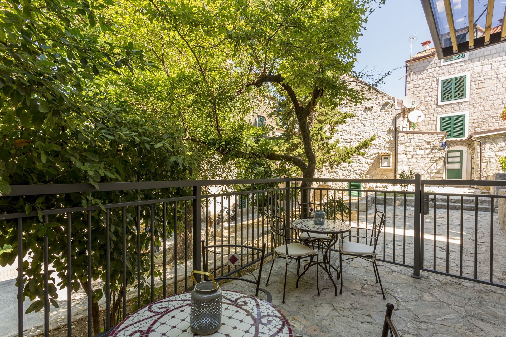 An outdoor seating area with a table and chairs, surrounded by a stone wall and a metal fence.