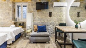 Ein Zimmer mit Steinwänden, einer Couch mit Kissen, einem Esstisch und einem an der Wand montierten Fernseher.