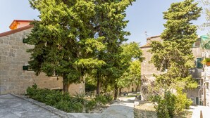 Ein Steinweg führt durch einen Innenhof mit Bäumen und Gebäuden.