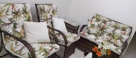 A room with two wicker chairs with floral upholstery, a small table, and a framed painting on the wall.