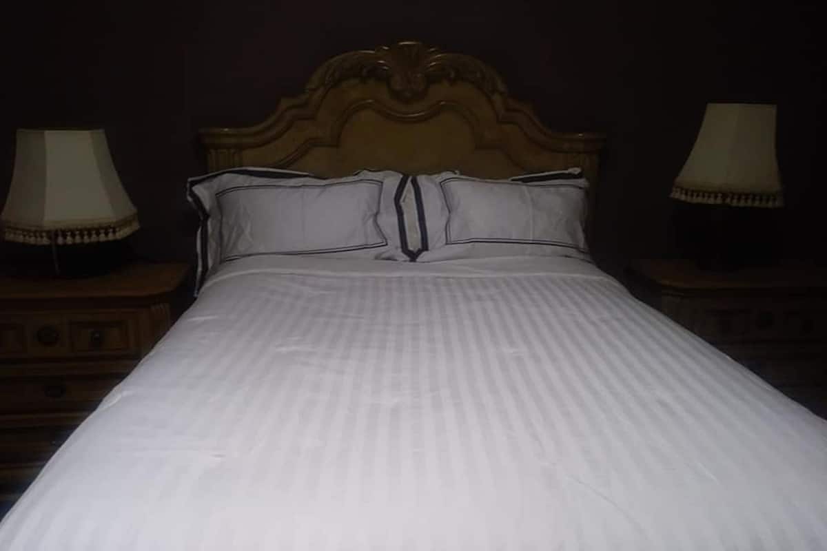 Een bed met een houten hoofdbord en twee nachtkastjes met lampen.