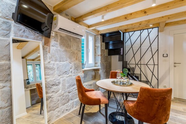 A dining area with a stone wall, wooden ceiling beams, and a round table with chairs. - Luxury Room Miara in Split City Center III (Split)