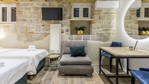 A cozy room with stone walls, a flat-screen TV, a wooden ceiling, a round mirror, a sofa, a dining table, and two beds. - Luxury Room Miara in Split City Center I (Split)