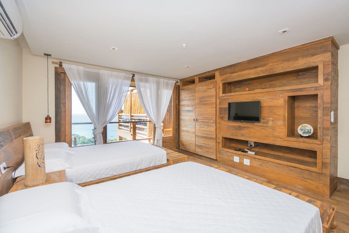Ein Schlafzimmer mit zwei Betten, einem Fernseher, Holzmöbeln und Meerblick.