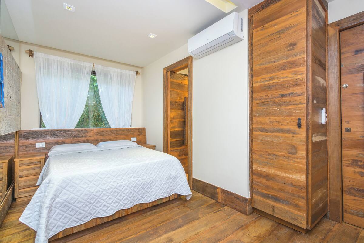 Ein Schlafzimmer mit einem hölzernen Bett, einem Holzschrank und einem Fenster mit transparenten Vorhängen.