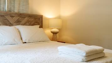 Una cama bien hecha con sábanas y almohadas blancas, una lámpara de noche y una toalla doblada sobre la cama.