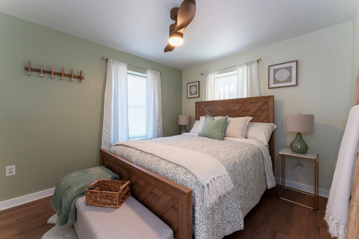 Un dormitorio con una cama de madera, una mesita de noche con una lámpara, un estante en la pared y una ventana con cortinas.