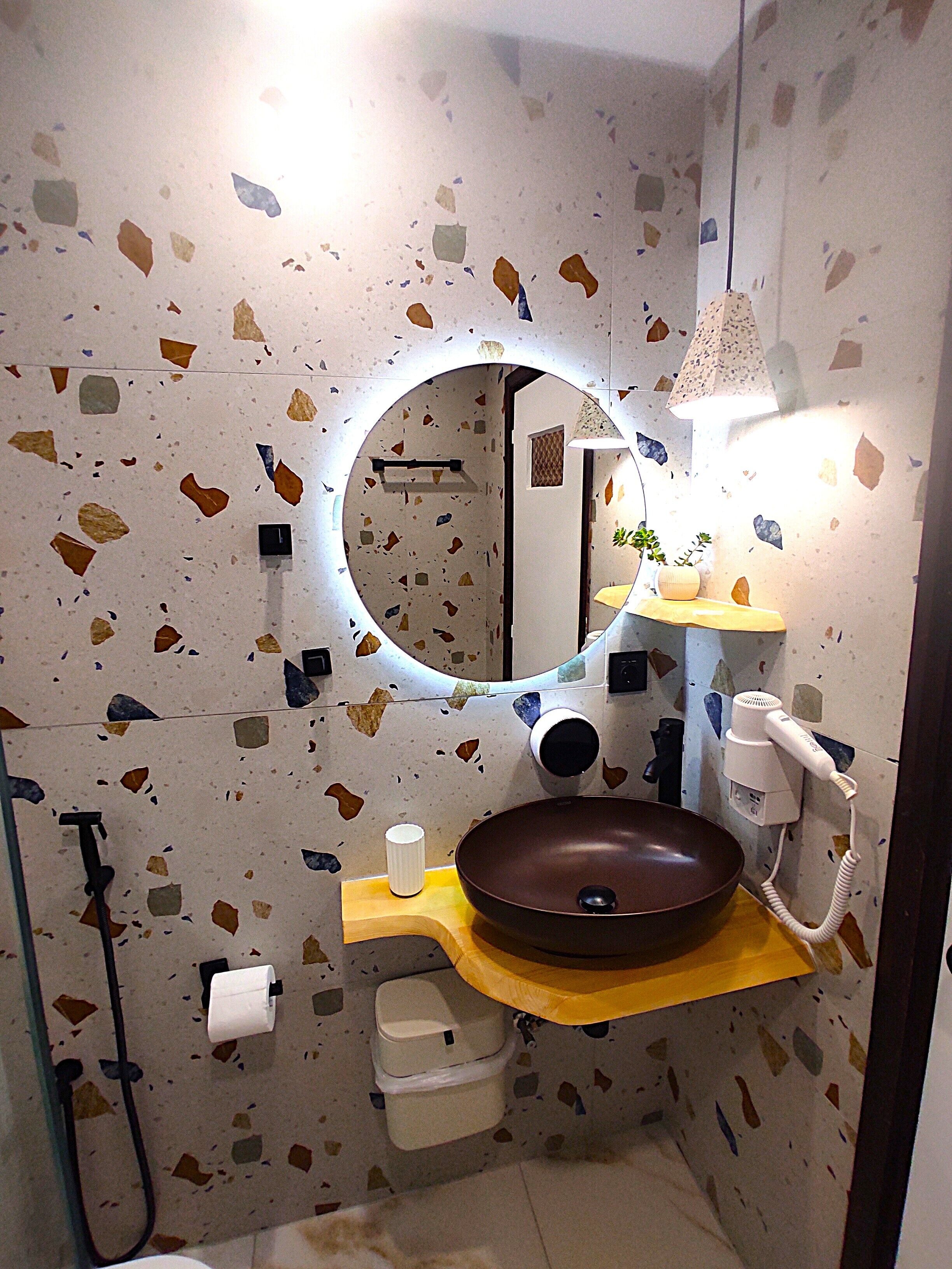 A bathroom with a round mirror, a brown sink, a towel rack, a toilet, and a hairdryer.
