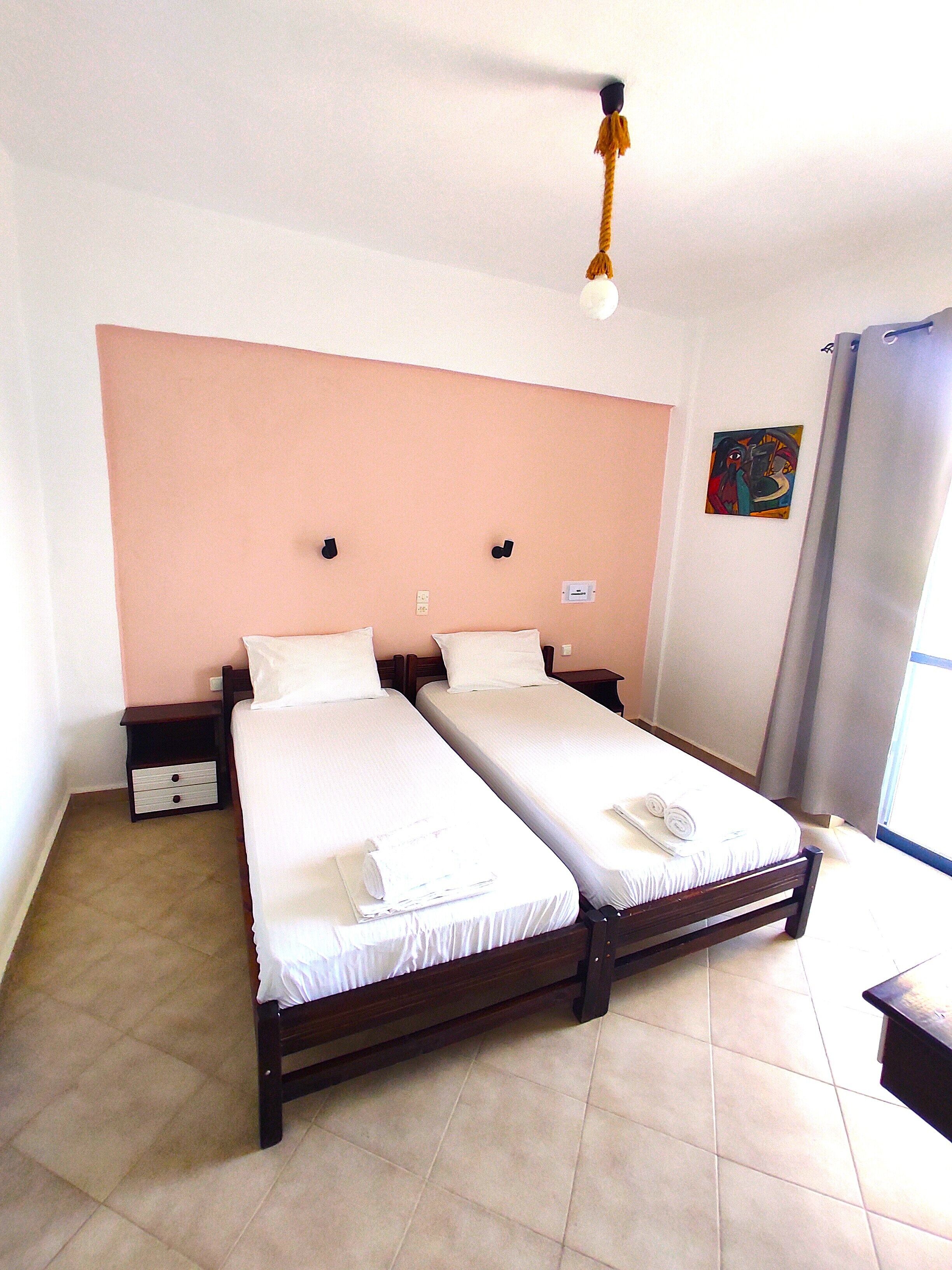 A double bed room with two single beds, a nightstand, and a small table.