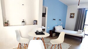 A modern living room with a dining area, featuring a marble-patterned rug, white furniture, and a blue accent wall. - Creta Star Apartments (Agios Vasileios)