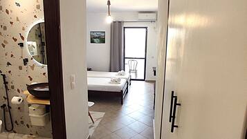 A hallway leading to a bedroom with a bed, a bathroom with a toilet and sink, and a shower area.