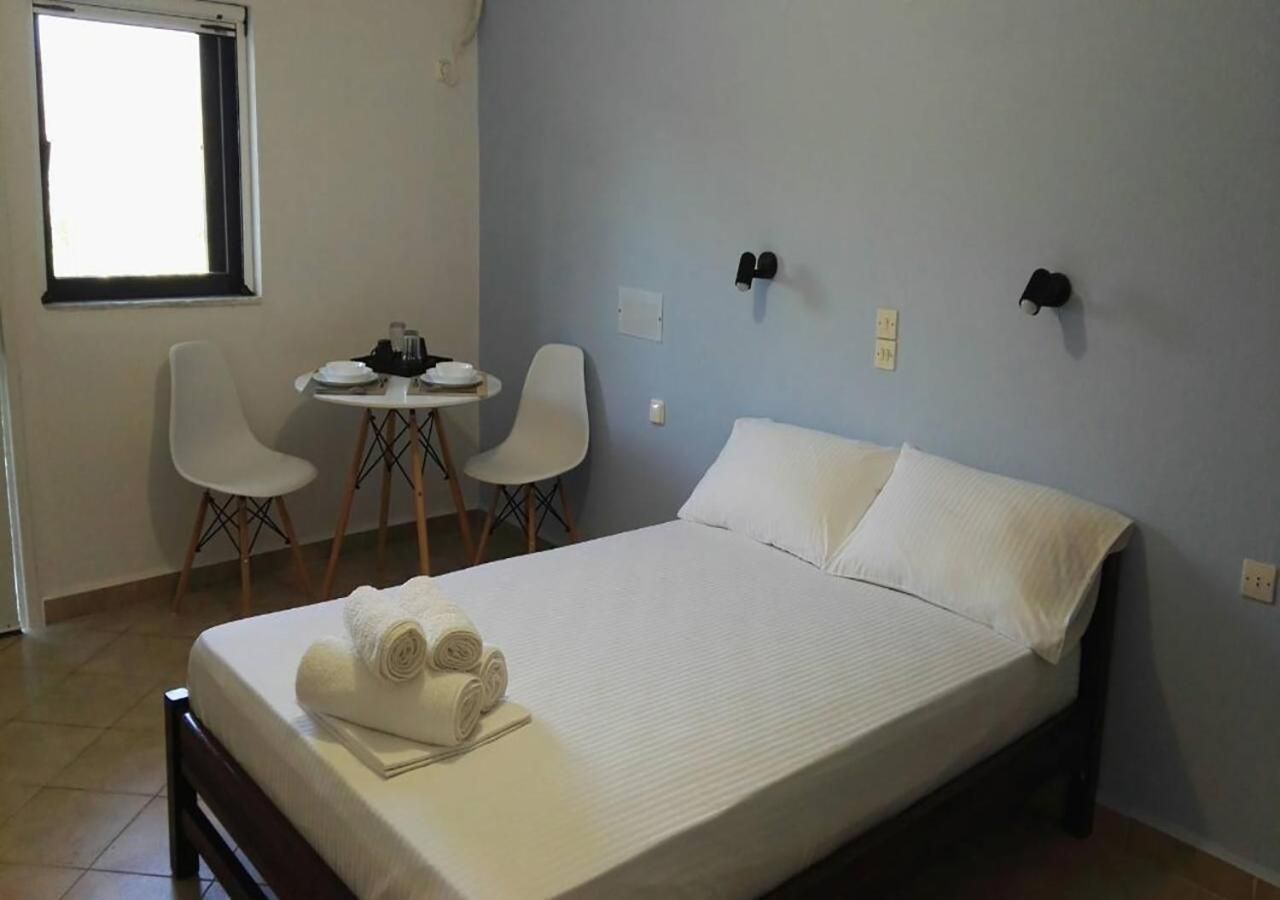 Un dormitorio con una cama, dos sillas, una mesita y un ventanal.