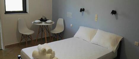 A bedroom with a bed, two chairs, a small table, and a window.