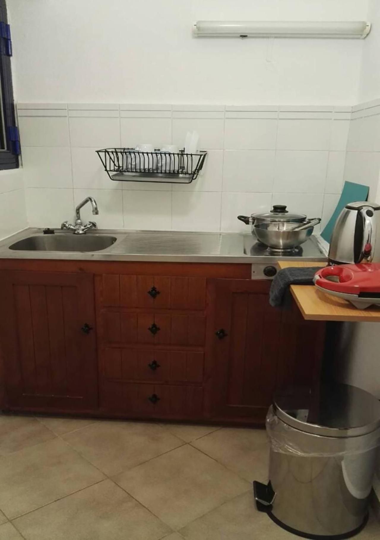 A kitchen with a sink, a stove, a kettle, and a trash bin.