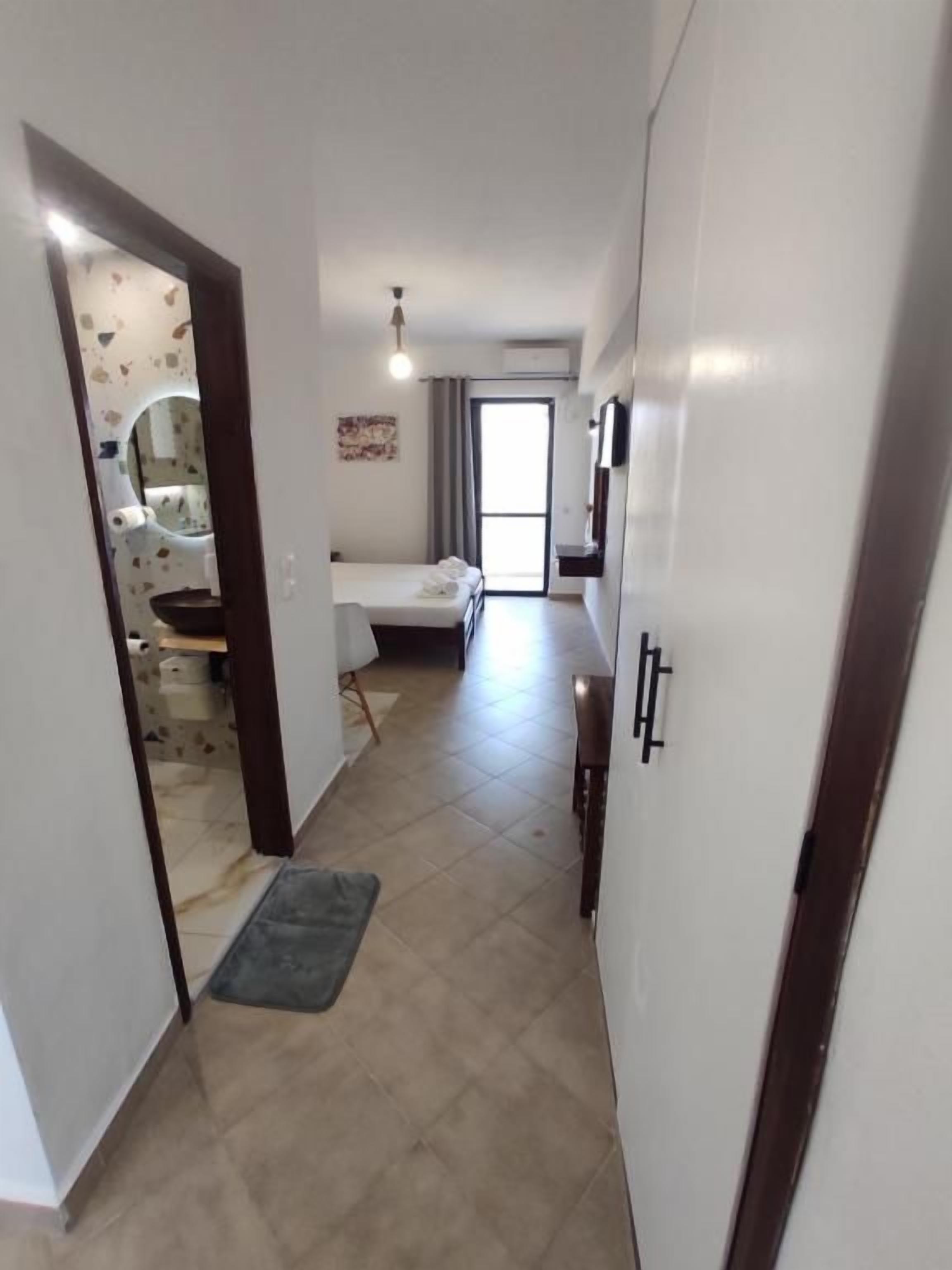 Un pasillo que conduce a un dormitorio con cama, ventana y puerta con espejo.