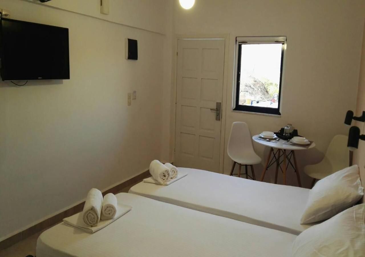 A hotel room with two beds, a TV, a small table with a chair, and a window.