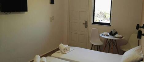 A hotel room with two beds, a TV, a small table with a chair, and a window.