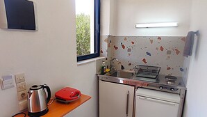 A compact kitchen with a window, a sink, a stove, a kettle, and a trash bin. - Creta Star Apartments (Agios Vasileios)