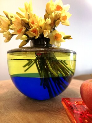 Un vaso di vetro trasparente con fiori gialli su un tavolo di legno.