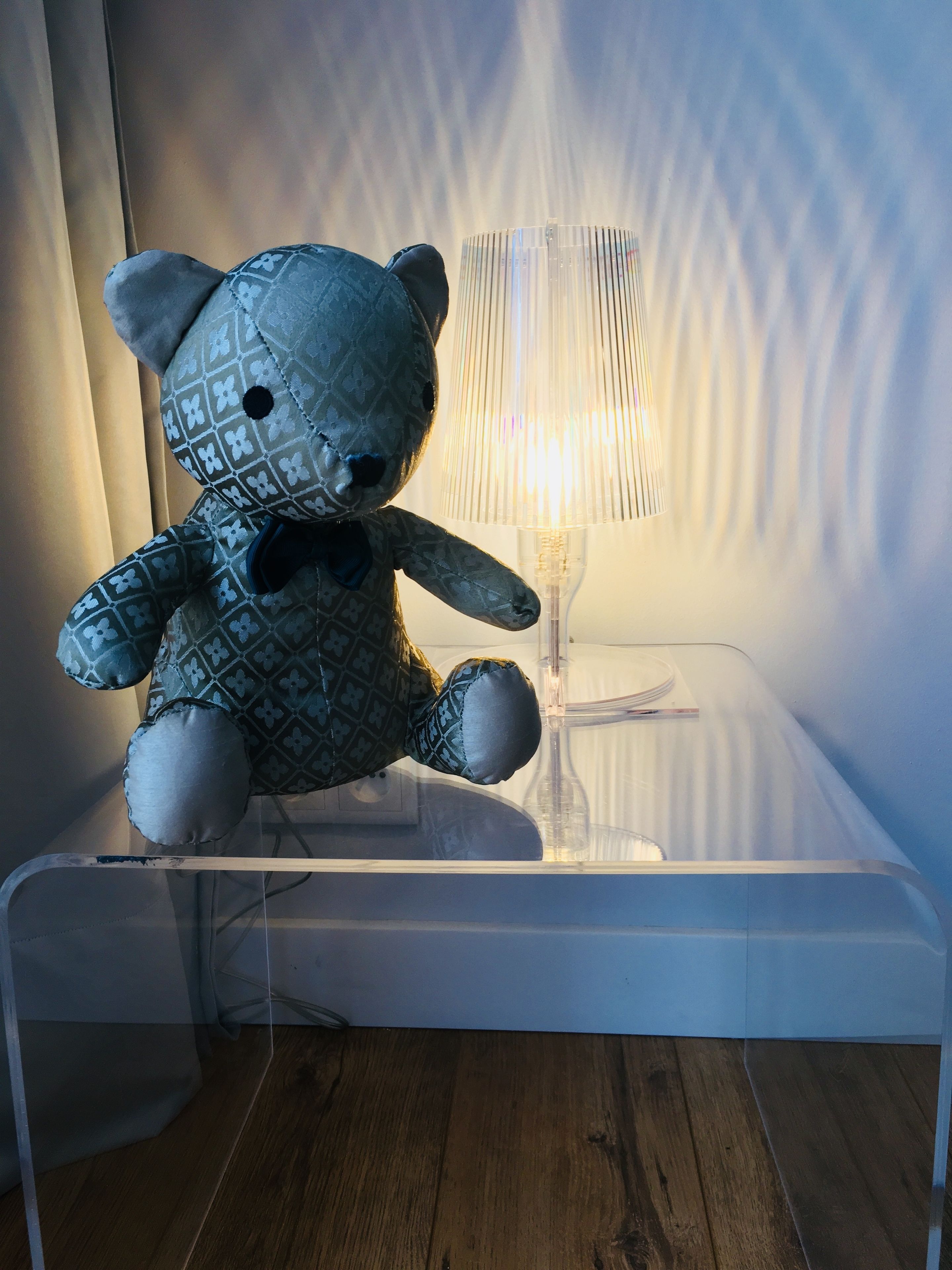 A plush toy on a clear glass table with a lamp in the background.