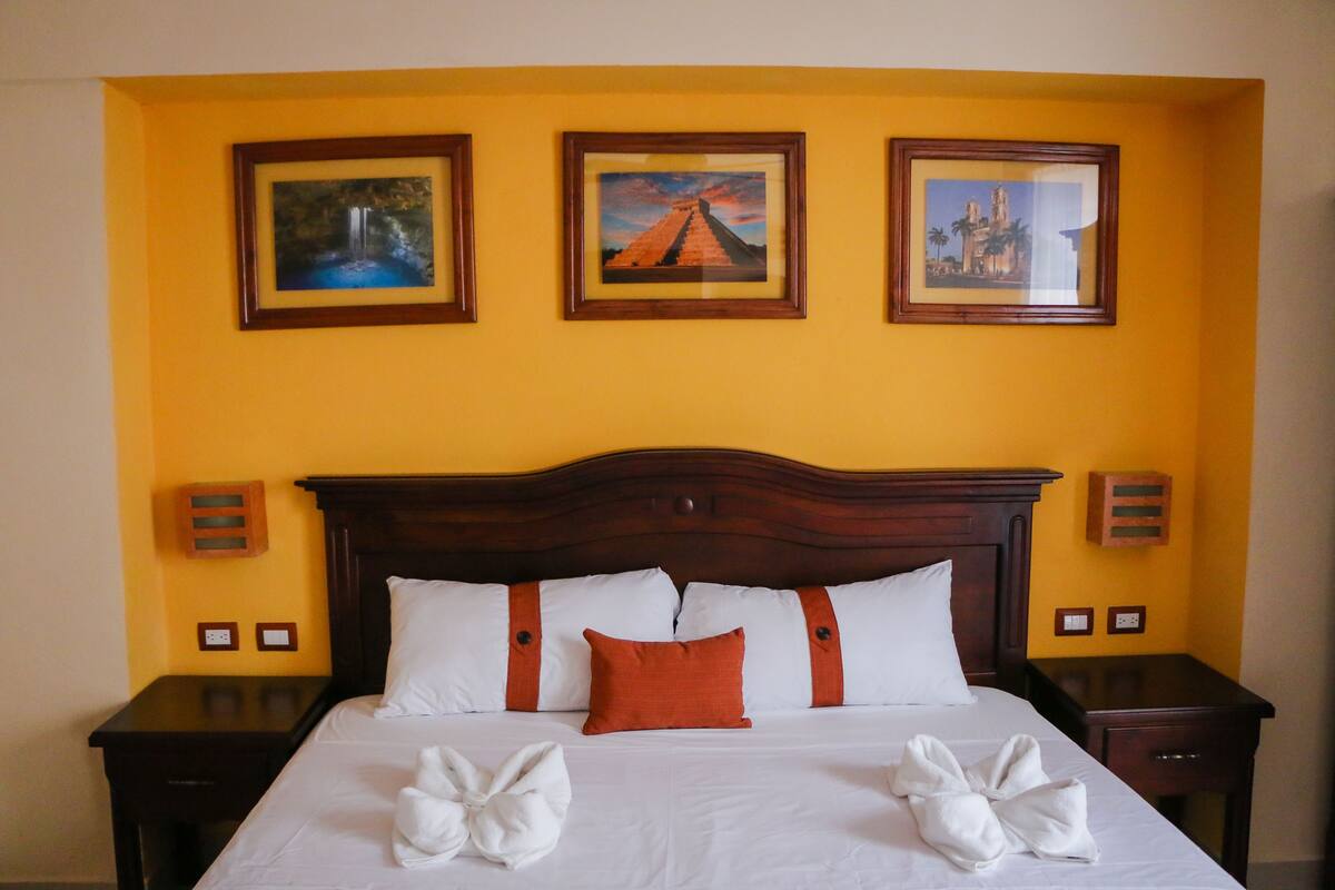 Une chambre d’hôtel avec un grand lit, une tête de lit en bois, du linge de lit blanc et trois tableaux encadrés accrochés au mur.