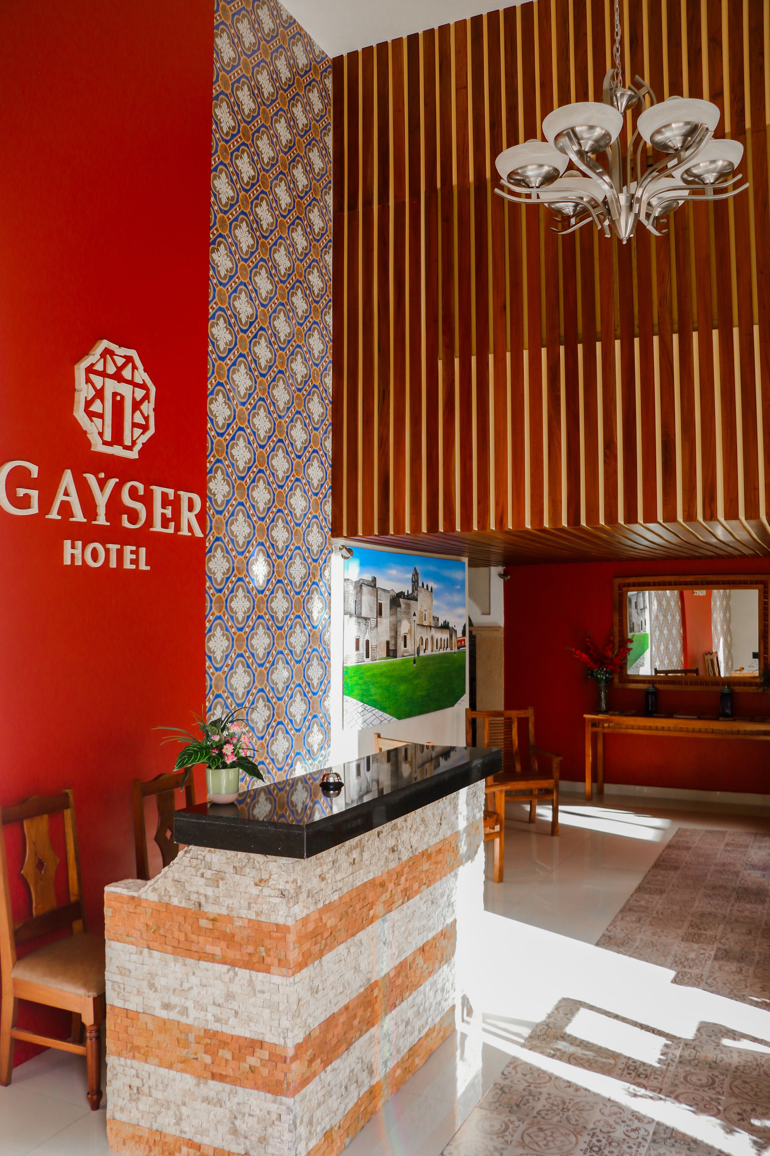 A reception area with a red wall, a patterned vertical panel, and a chandelier.