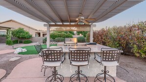 An outdoor patio with a grill, three chairs, and a pergola with a ceiling fan. - Club Wolff  West - Enjoy Tucson in Style.  Pool, hot tub, outdoor kitchen, view (Tucson)