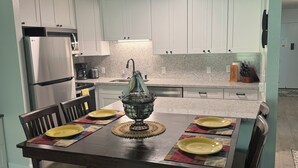 Una cocina moderna con armarios blancos, un refrigerador de acero inoxidable y una mesa de comedor con platos amarillos y un centro de mesa decorativo.