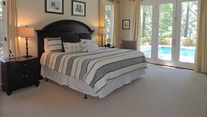 Une chambre spacieuse avec un grand lit, deux tables de chevet avec des lampes, un ventilateur de plafond et une vue sur une piscine, visible à travers les portes vitrées.
