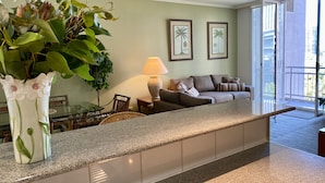 A modern living room with a kitchen counter, a dining table, a sofa, and a large window with a view of the city. - Riverside. Walk to Crown, CBD & MCG. Free Secure Carpark. (MELBOURNE)