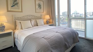 A hotel room with a large bed, two bedside tables with lamps, a city view through large windows, and artwork on the walls. - Riverside. Walk to Crown, CBD & MCG. Free Secure Carpark. (MELBOURNE)