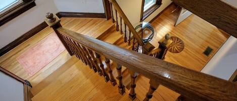 Uma escada de madeira com corrimão, que leva a um quarto com piso de madeira e uma pequena mesa redonda.