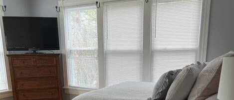 Un dormitorio con cama, cómoda, televisión y ventanas.