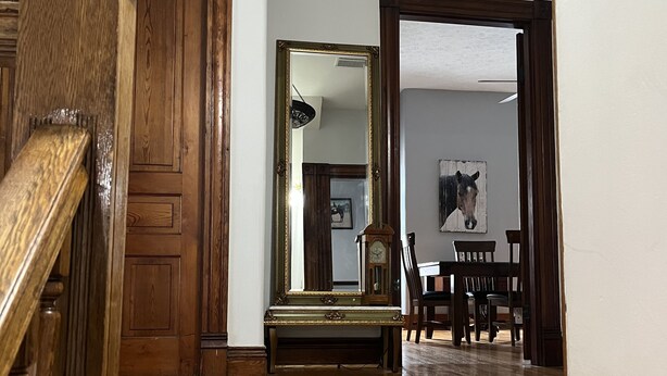 A wooden staircase leading to a room with a wooden floor, a mirror, a clock, and a painting on the wall.