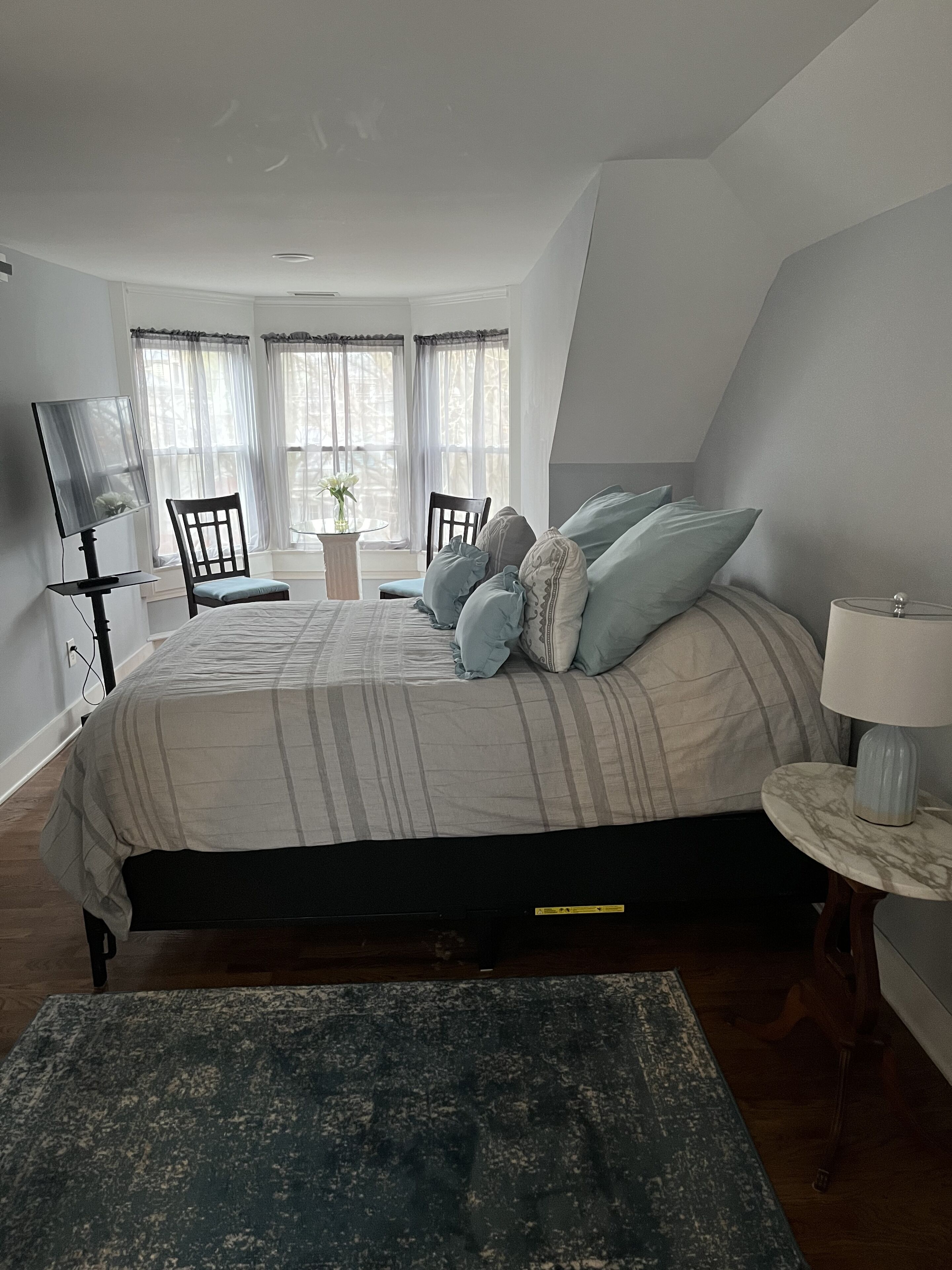 Un dormitorio con cama, televisor, escritorio y ventana con cortinas.