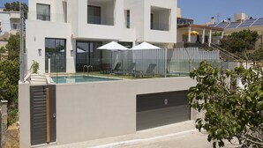 A modern two-story house with a swimming pool, a covered patio with umbrellas, and a garage.