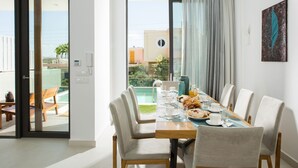 A dining area with a view of a pool and buildings, a table set with plates, glasses, and a vase.