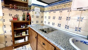 Una cocina con encimera de granito, un fregadero y una estufa. Se observa una estantería con vajilla y un armario con electrodomésticos de cocina.