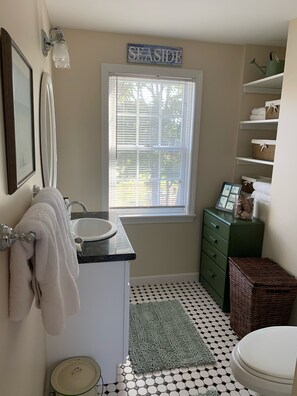 A bathroom with a white sink, a toilet, a window with blinds, a green cabinet, and a 'SEASIDE' sign. - Cozy Efficiency with Beautiful Ocean Views (Orrs Island)