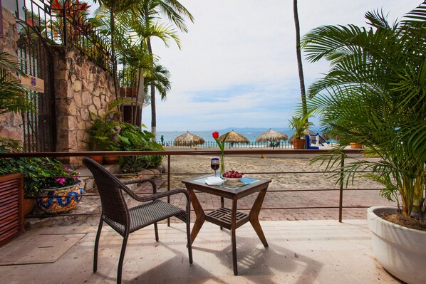 Relax on the terrace with a view of the beach, featuring a wicker chair, table, and potted plants.