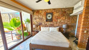 Ein Schlafzimmer mit Steinwand, einem Bett mit weißem Überwurf, zwei Nachttischlampen und einem Deckenventilator.
