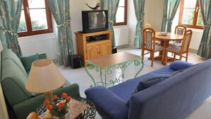 En stue med sofa, lille bord med lampe, fjernsyn på træstel og spisebord med stole.