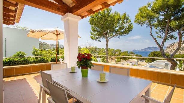 Une terrasse avec une table et des chaises, un pot de fleurs et une vue sur la mer et les collines.