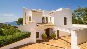 Une villa blanche de style méditerranéen, dotée d’un toit en tuiles, d’un patio couvert et offrant une vue sur la mer.