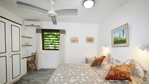 Een slaapkamer met een bed, een bureau, een stoel, een plafondventilator en een raam met gordijnen.