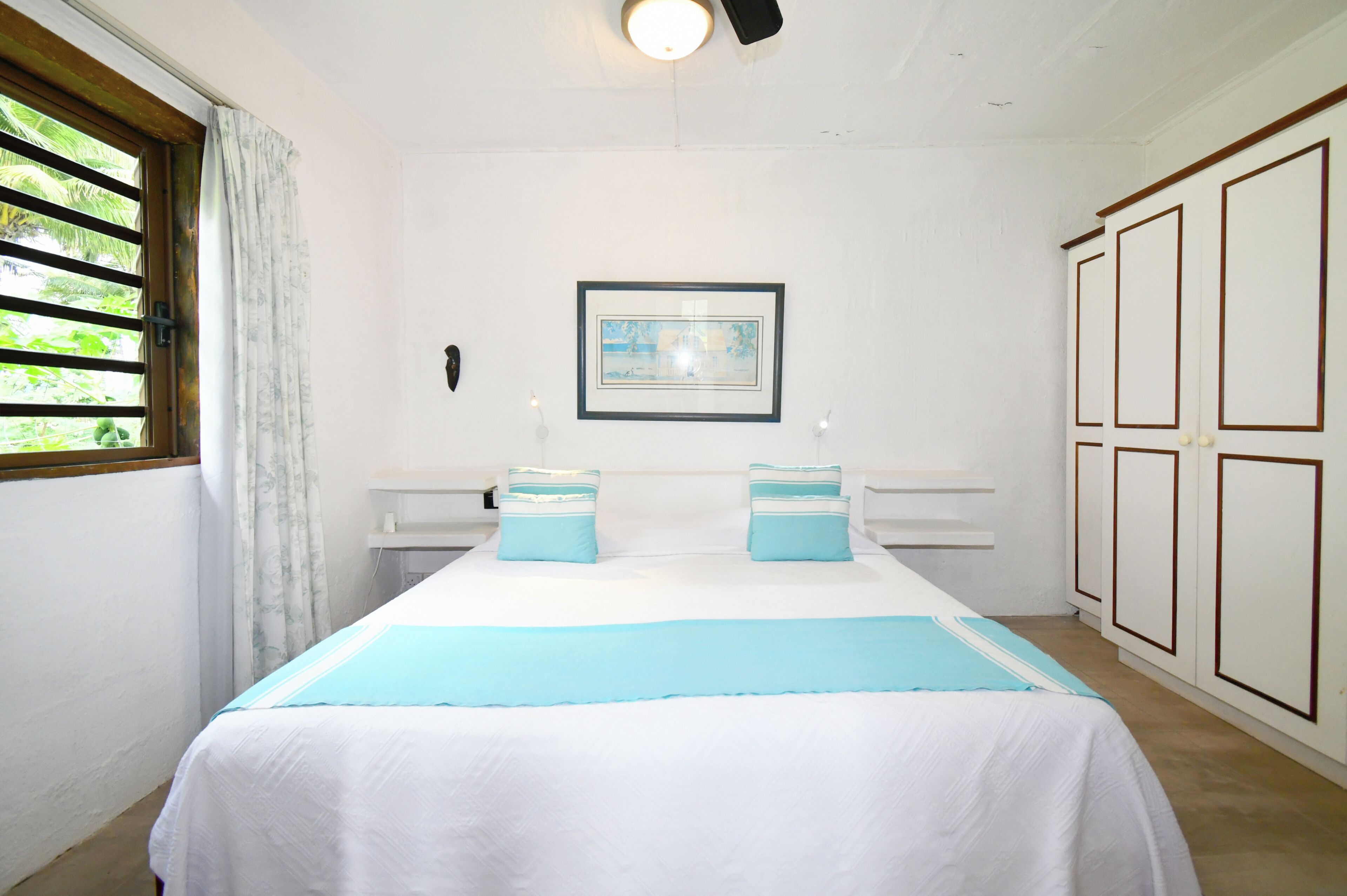 A bedroom with a bed, a framed picture on the wall, and a window with curtains.