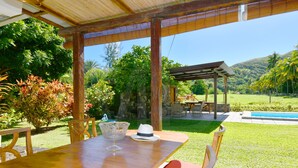 Een terras buiten met een houten tafel en stoelen, een glazen schaal en een hoed.