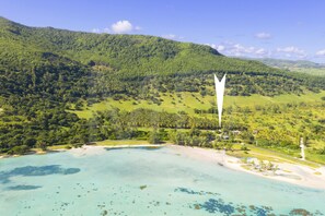 Un paysage côtier avec une plage, une végétation luxuriante et un ciel dégagé.