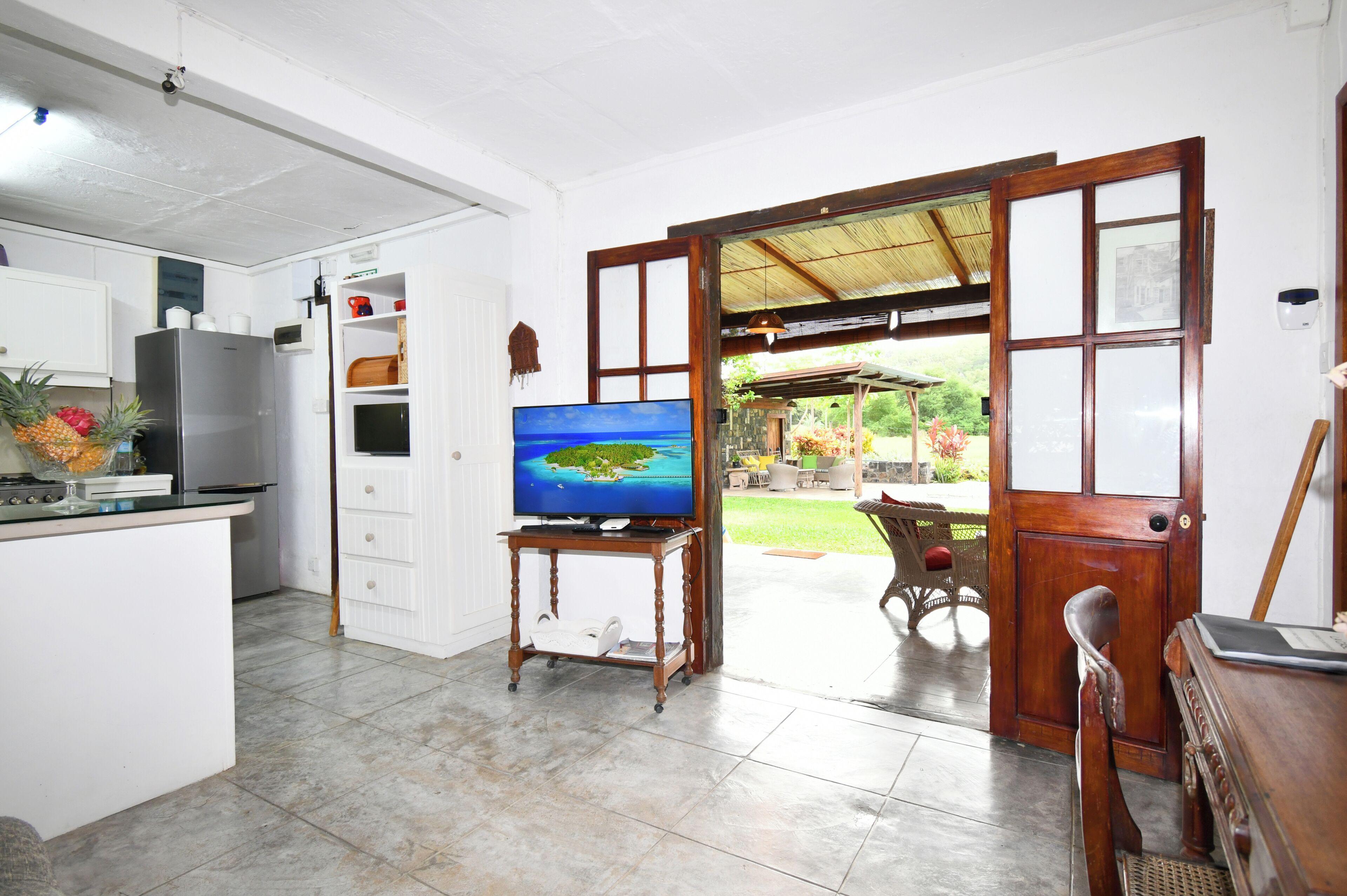 A kitchen with a refrigerator, a dining area with a table and chairs, and a television on a stand.