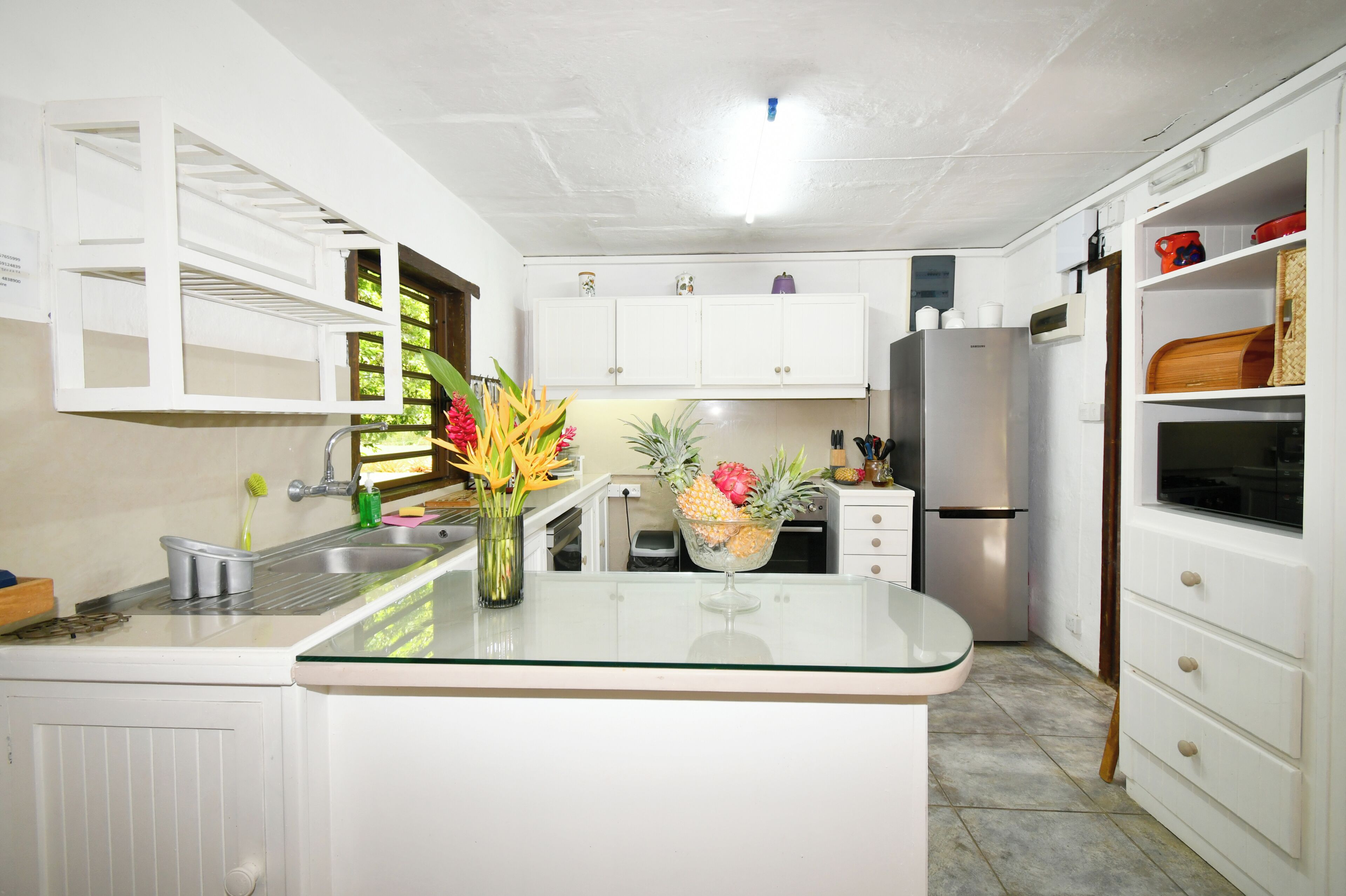 A modern kitchen with white cabinetry, a stainless steel refrigerator, and a glass island with a vase of flowers.